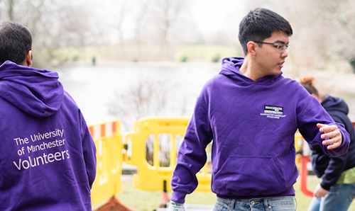 Two students wearing purple hoodies, volunteering in a field